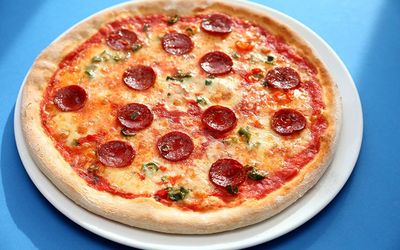 Pepperoni pizza served on a large white plate on a blue table.