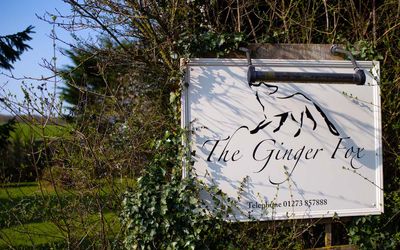 The Ginger Fox sign with foliage around it on a sunny day.
