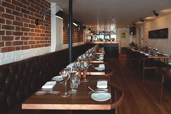 Gingerman Brighton. Wooden tables, brick walls, a minimalist interior with glasses on the table waiting for service. 