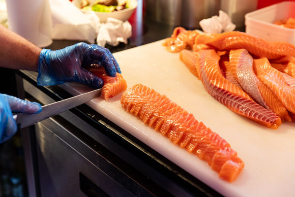a chopping board with salmon being chopped into sushi slices