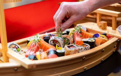 hand adding final touches to a small wooden boat filled with sushi