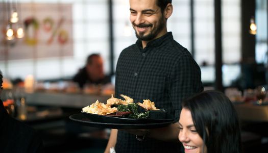 waiter serving sushi dishes. he is dressed in black, with the japanese style seating behind hi. This is Moshimo Brighton
