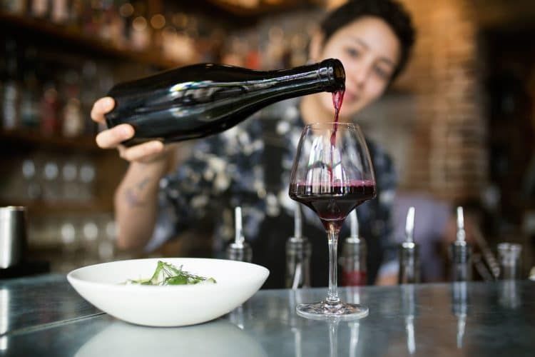 Bartender pouring a glass of red wine at the bar with a bowl of food ready to be served. Best bars in Brighton. wine bar brighton