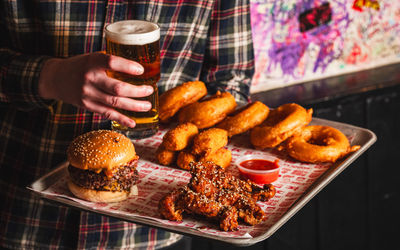 Meatliquor - a person holding tray with delicious food from Meatliquor including fried meat, burgers, onion rings and glass of beer.