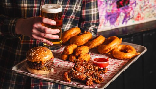 Meatliquor - a person holding tray with delicious food from Meatliquor including fried meat, burgers, onion rings and glass of beer.