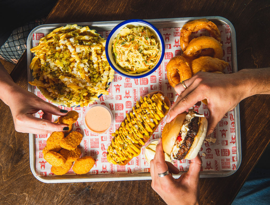 over head shot of the food tray and two people eating delicious food of it, including burger, onion rings, nuggets, fries and salad. This is where to eat in Brighton. Positioned on London Road Brighton. Brighton Food photography, picture taken by Ellen Richardson. Featured in our Halal restaurants in Brighton guide