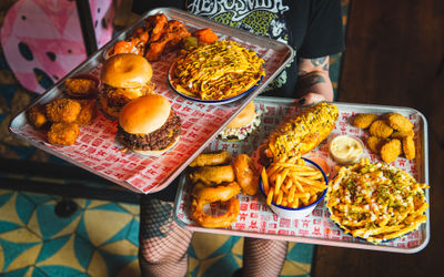 Brighton waiter holding two big trays filled with burgers, fries, hot dog, nuggets and onion rings. Brighton food available for Brighton takeaway. Meatliquor is close to Brighton Open Market