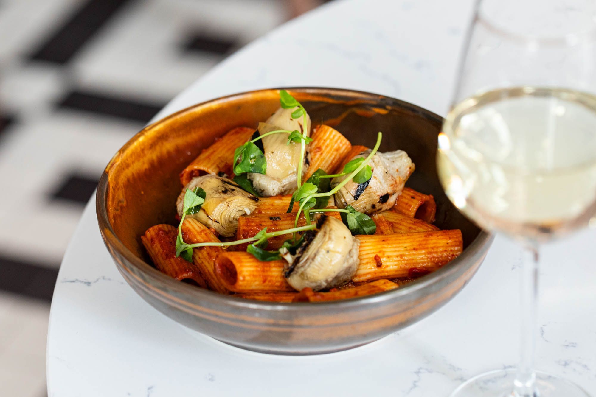 pasta with vegetables in brown bowl and served with glass of white wine at metropole bae