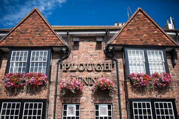 Exterior of The Plough Inn on a sunny day with clear skies an pink hanging baskets