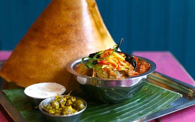 Colourful Indian food served on a leaf and in metal bowls.