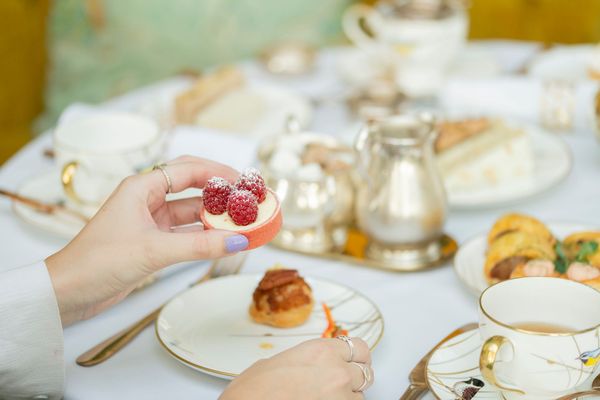 hand holding small round cake with raspberry on the top of it. Afternoon tea at The Grand