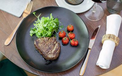 black plate with the steak, piece of salad and cherri tomates