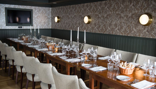 large dining room with patterened silver wallpaper. A wooden table with dinner settings and candelabras in place. Light leather chairs surround the table. Meetings Rooms Brighton