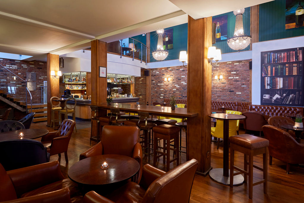 A warm bar with leather seats, exposed brick walls and chandeliers. Bar stools in foreground.