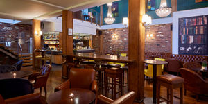 A warm bar with leather seats, exposed brick walls and chandeliers. Bar stools in foreground.