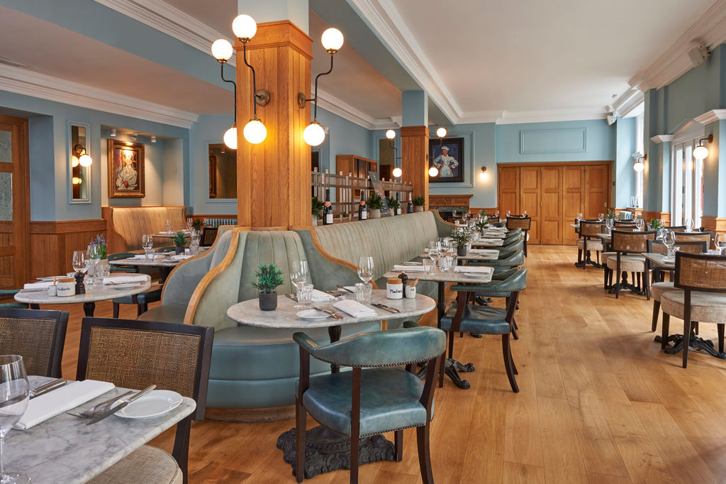 a large duck egg blue dining rooms with several tables and chairs with banquetter seating in the centre. The floor is wooden and the tabletops are marble. Boutique Hotels Brighton guide.