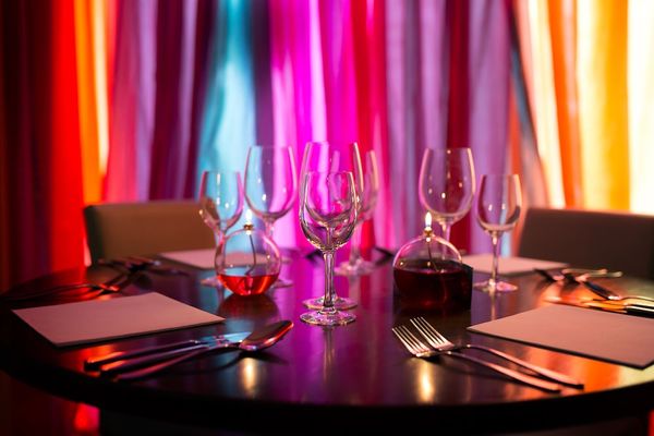 Interior at Indian Summer, a table dressed with wine glasses and menus with a multi coloured fabric backdrop.