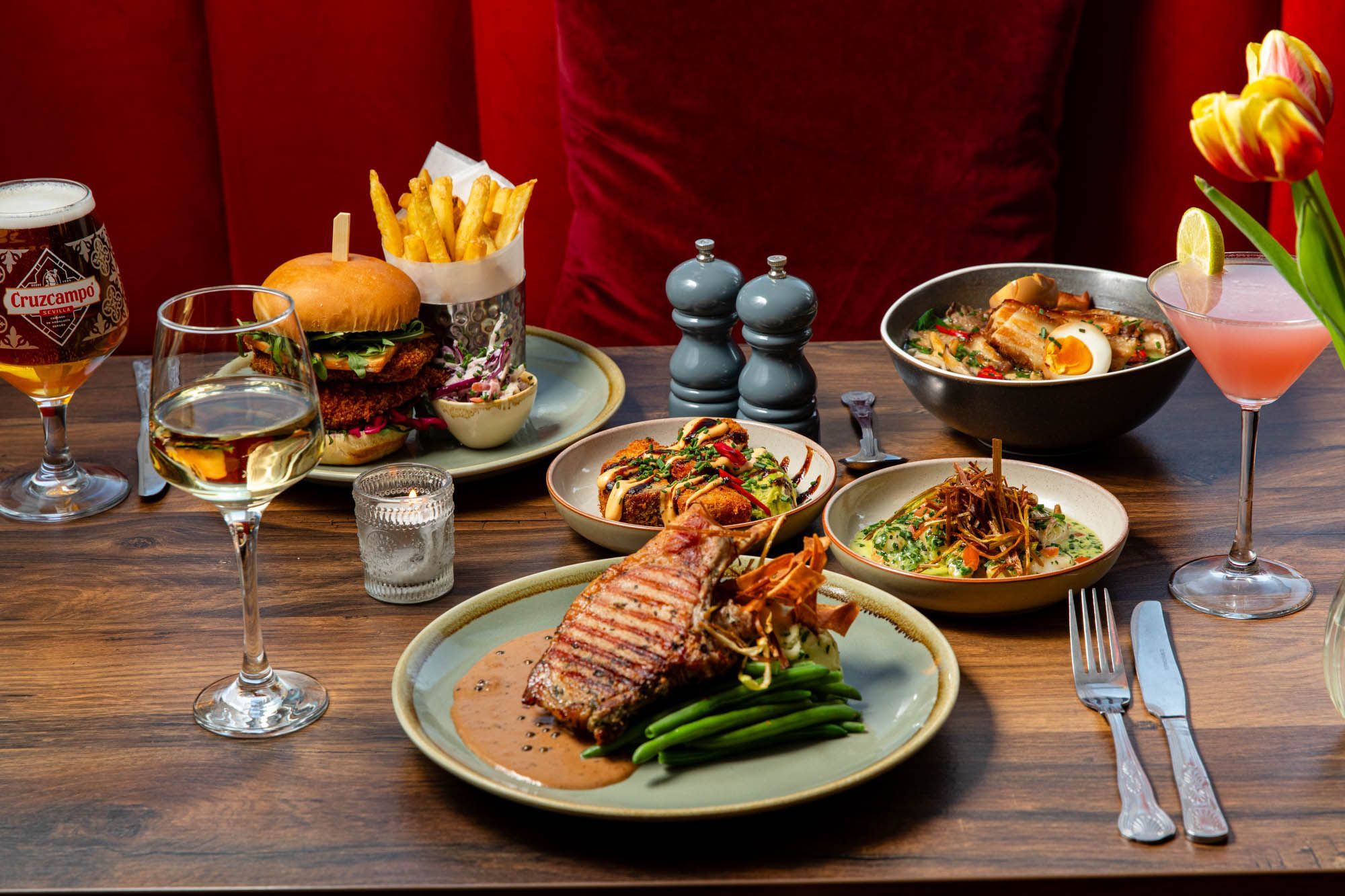 side shot of the Chimney House table laid out for three people with various lunch dishses inluding burger and chips, egg and meat bowl, sides and cocktails