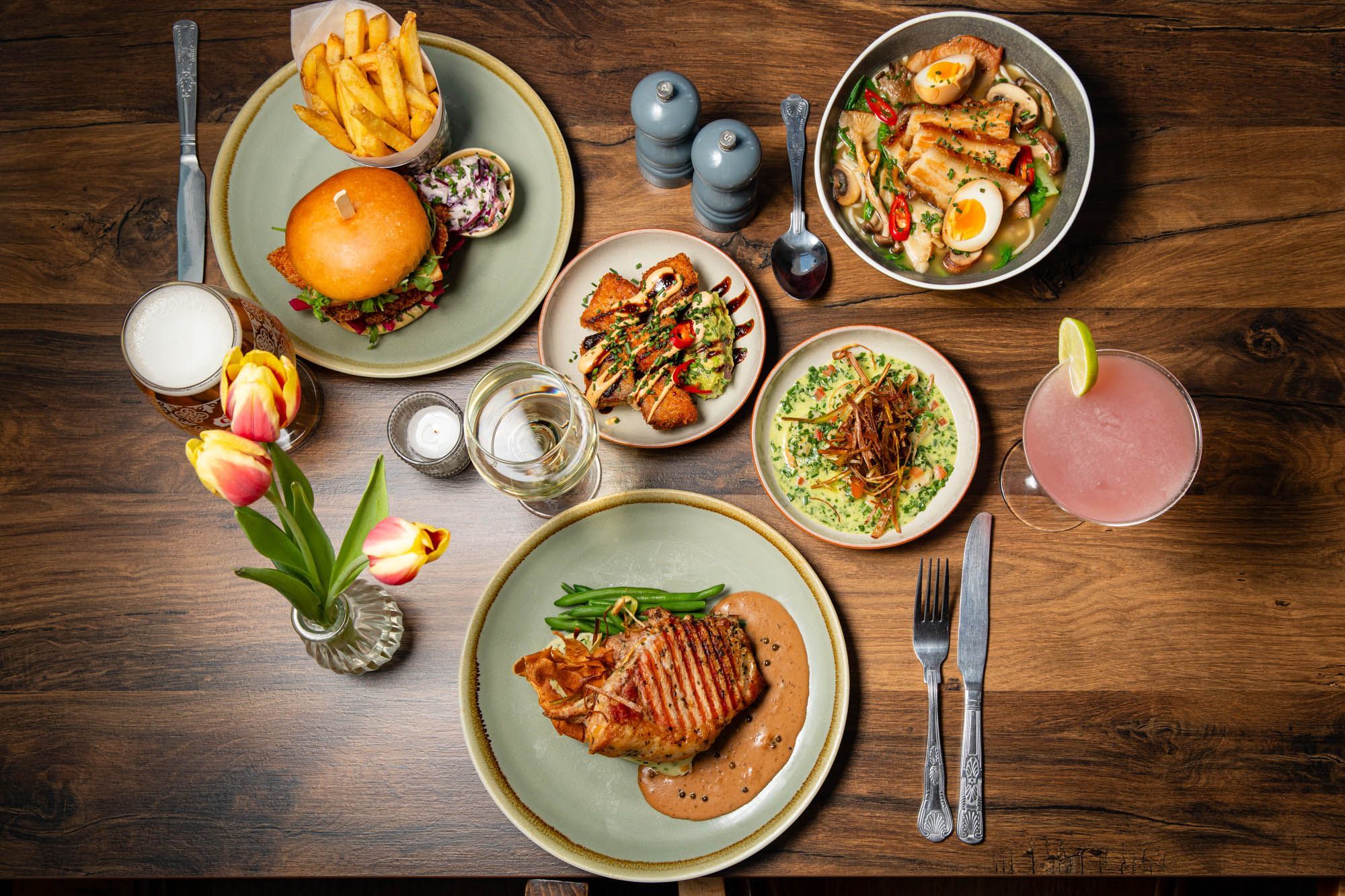 over head shot of the Chimney House table laid out for three people with various lunch dishses inluding burger and chips, egg and meat bowl, sides and cocktails