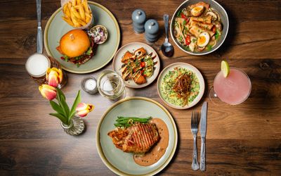 over head shot of the Chimney House table laid out for three people with various lunch dishses inluding burger and chips, egg and meat bowl, sides and cocktails