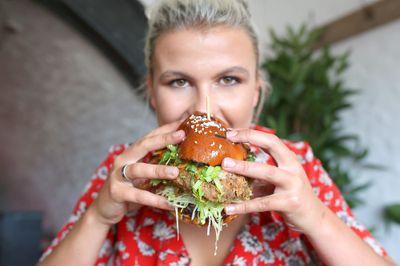 A crispy burger with shredded lettuce in a seeded bun being eaten by a person in a red dress.