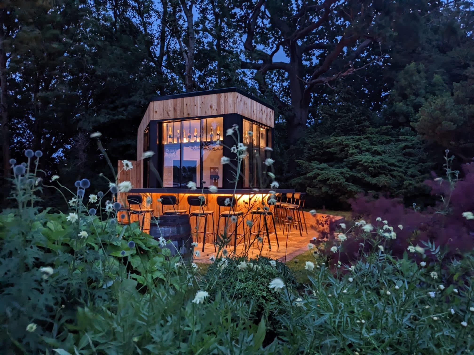 Pictured, a well lit garden bar nestled among the trees in the South Downs