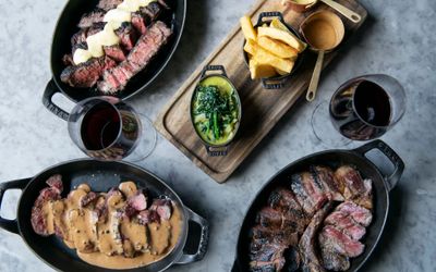 table laid out with prime cut meat dishes in black metal dishes. a side of chips and cheesey broccolli on a wooden board. A lunch in Brighton of epic proportions. Located in the Lanes Brighton