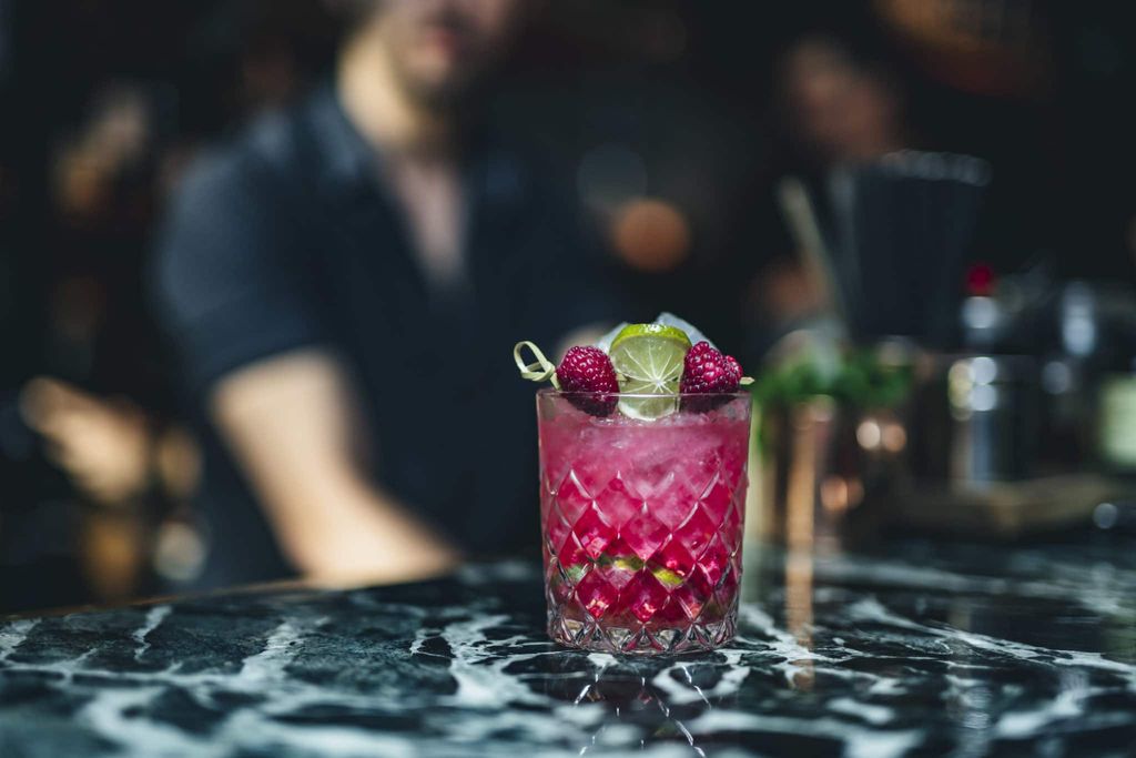 a colourful cocktail with Raspberries. This is an alcohol free cocktail. the drink is sitting on a marble bar which is black and grey in colour.
