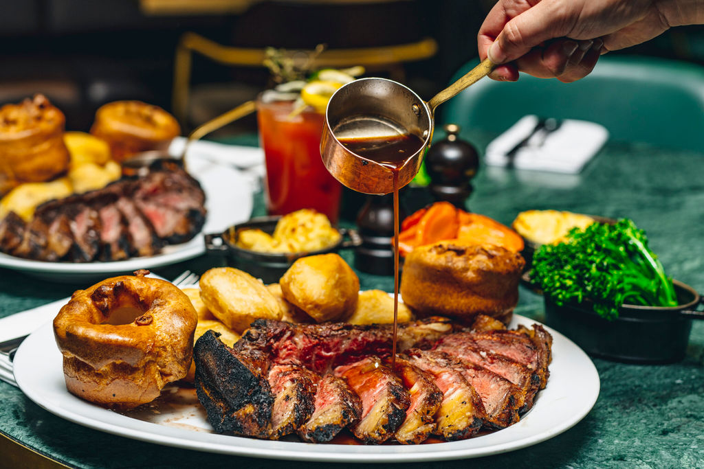 A plate of steak with Yorkshire puddings, roast potatoes, vegetables and gravy being poured over it