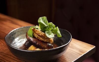 A rustic black bowl with sausages and mashed potato topped with fresh watercress.