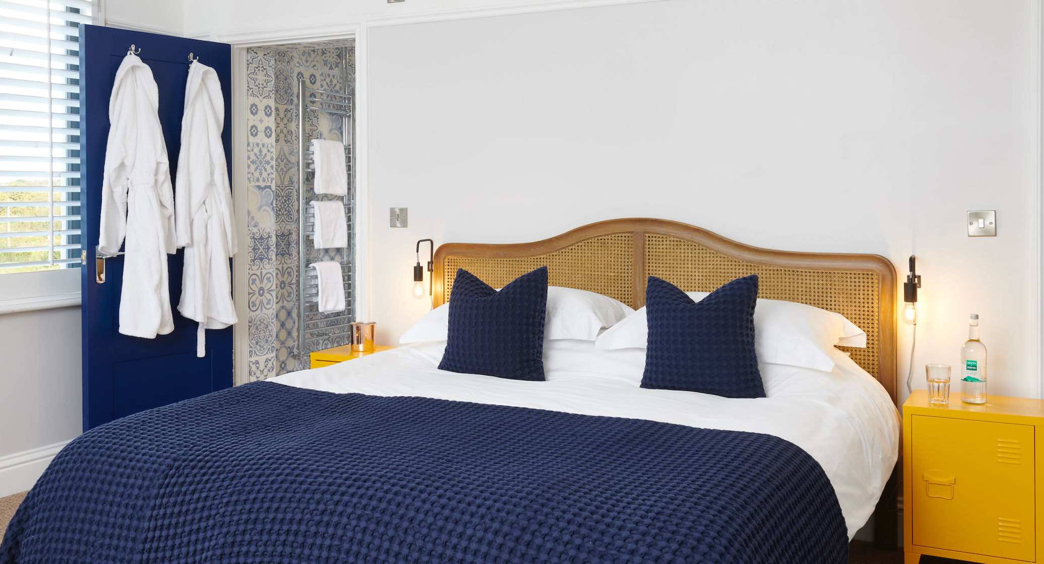 a bright airy bed and breakfast with white sheets on a double bed with navy blue throws and pillows