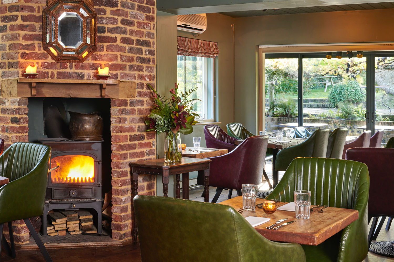 The interior of the Jolly Sportsman, a roaring fire, red brick walls and a backdrop of the conservatory dining area to their garden