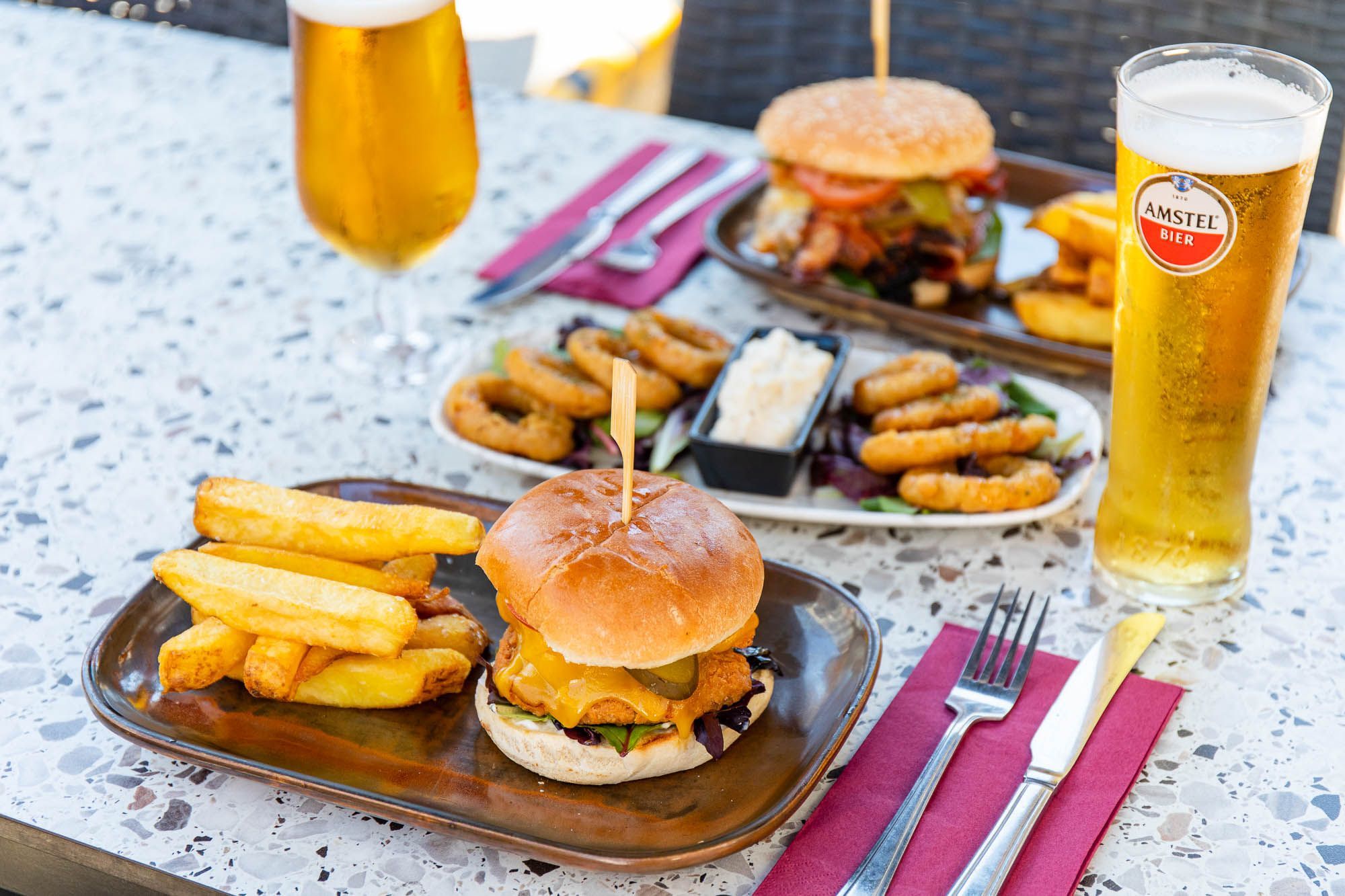 two boards with the burgers and chips, served with some onion rings, sauce and glasses of beer