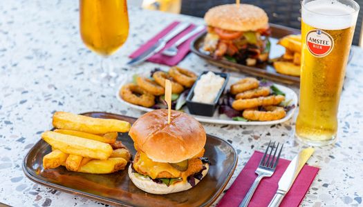 two boards with the burgers and chips, served with some onion rings, sauce and glasses of beer