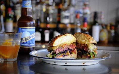 A photo of a slider cut in half on a bar with a bottle of Blue Moon beer and drinks in the background.