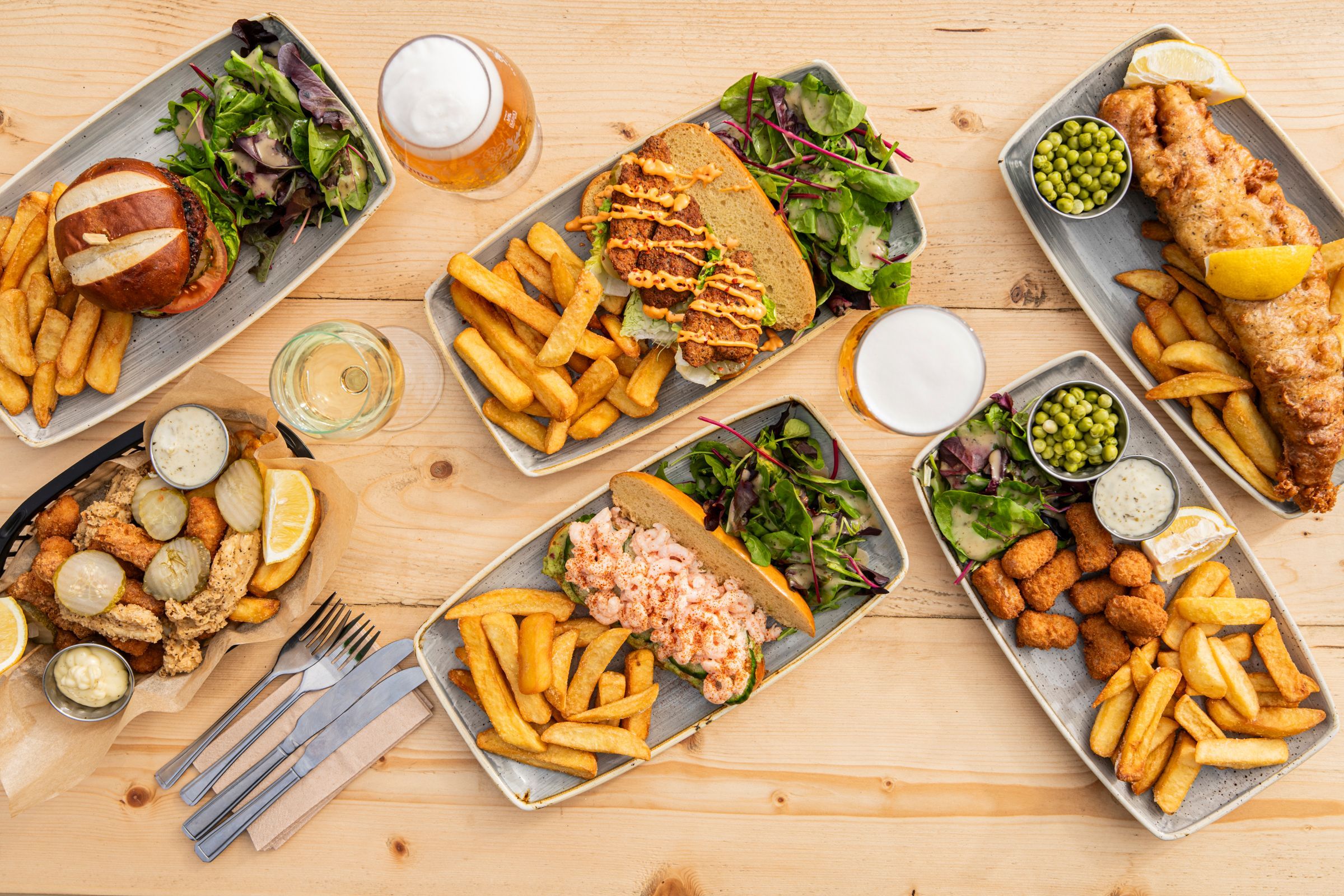 over head shots of six dishes served on the wooden table at Ohso, including burger and chips, fish and chips and beer