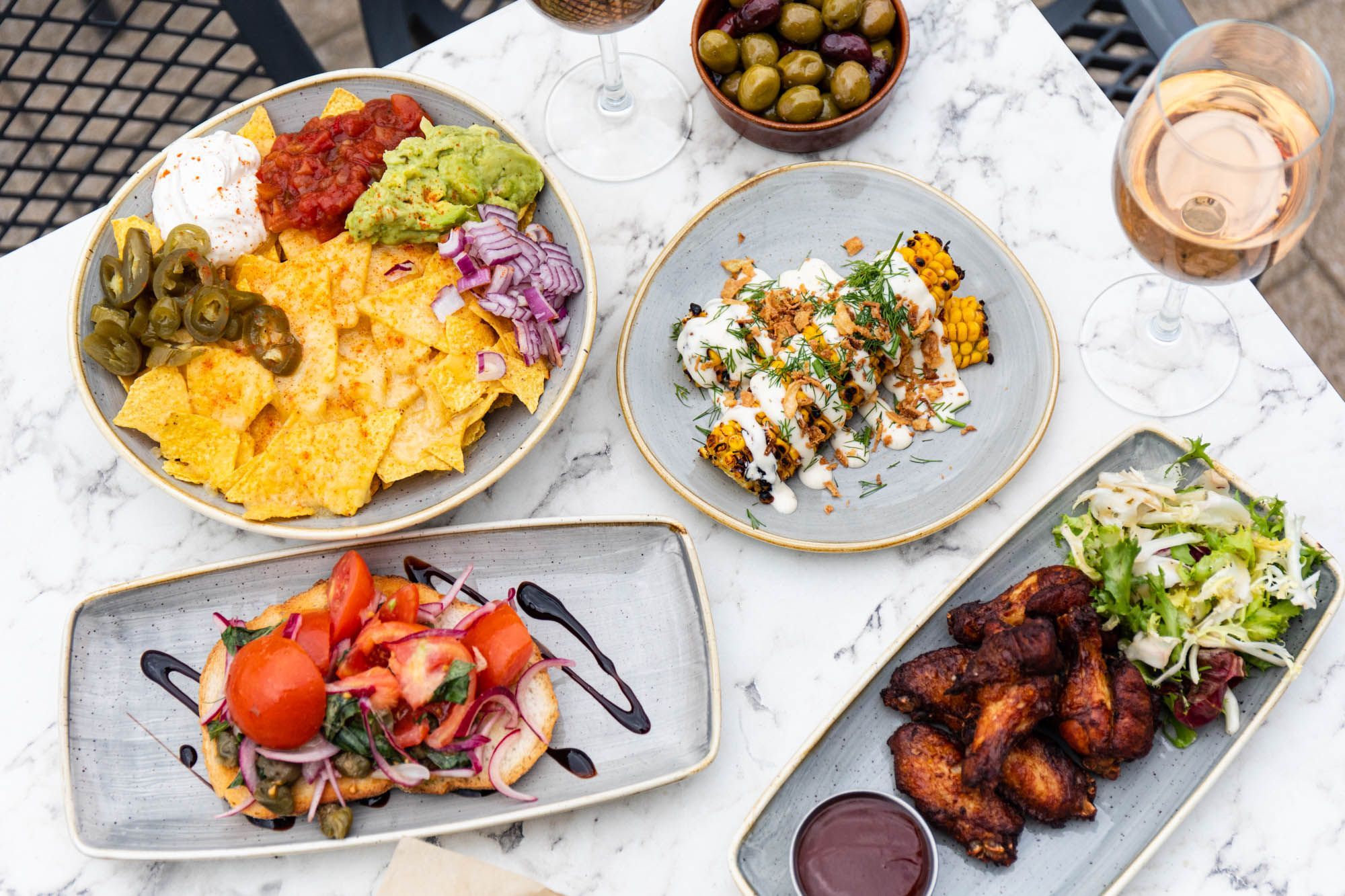 over head shot of the dishes including corn dish, tortilla chips with sauce, chicken wings. all served on the marble table at Ohso Brighton