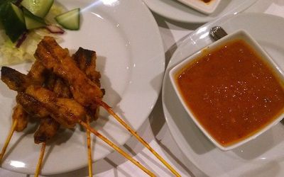 Plates of chicken satay skewers with dipping sauce and side salad