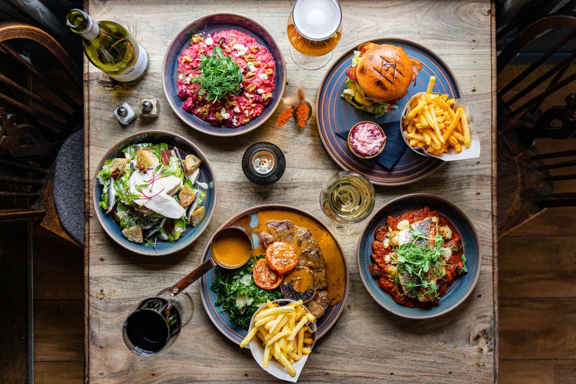 over head shot of the five different dishes served on the wooden table and with glasses of wine