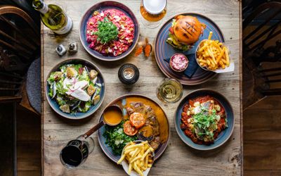 over head shot of the five different dishes served on the wooden table and with glasses of wine