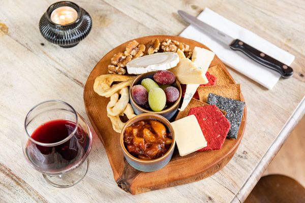 over head shot of the brown wooden board with charcuterie, cheese, crackers and dry fruits on, served with glass of red wine at The Sportsman Pub