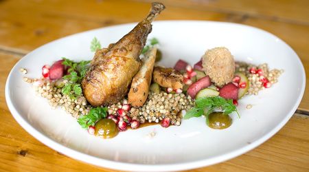 Pheasant served with bulgur wheat and pomegranates on a large white oval plate.