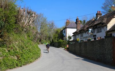 Cyclists riding along a country lane passed the pub on a bright Summers day. Pubs in Sussex, Sussex Downs National Park.