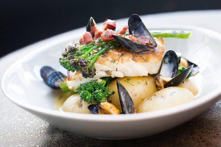 Cod main course with broccoli and mussels served in a white bowl