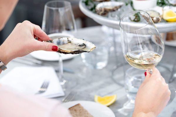 left hend holding oyster right hand holding glass of white wine