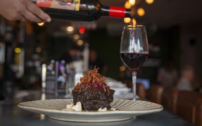 Market Restaurant. Wine bar Brighton and Hove. Pictured, a waiter pouring red wine into a glass while a customer sits at the barside. In the foreground ox cheeks presented on a white plate.