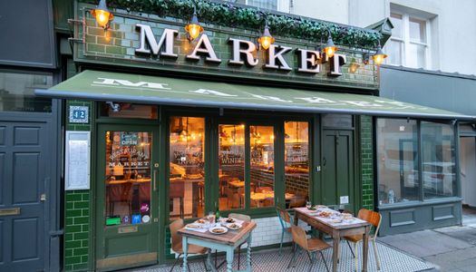 Green coloured entrance at market restaurant which is on Church Road in Hove. Voted 13th among the best restaurants in Brighton in 2023 at the Brighton restaurant awards. Market restaurant is described as Anglo-Spanish tapas and provides you with a social dining experience where you can watch the chefs at work. the sign above the restaurant is rescued from Camden market and the dining experience gives you the butcher, the fishmonger and the baker as part of the dining choices. the venue is owned by Neil Mannifield or Manni.