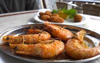 Garlic king prawns served on a plate with a side dish in the background. Fish Brighton Restaurant, seafood restaurant.