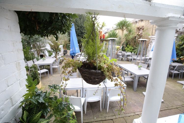 A beer garden with white furnishings and lots of plants. Brighton Beer Garden at Hove Place. Part of our Brighton Nightlife guide