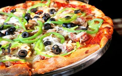 Close up photograph of an olive and green pepper pizza
